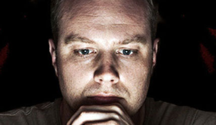 Image of a mans face lit up by a computer screen looking intently at it in colour